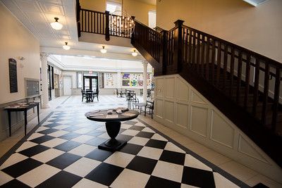 A grand interior hall with a black-and-white checkered floor, a central round table, and a dark wooden staircase.