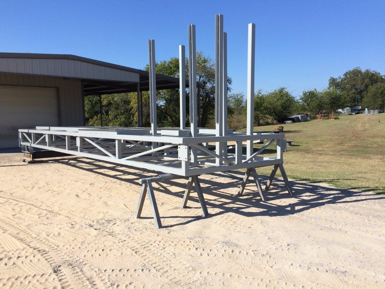 A large metal structure is sitting on a dirt road in front of a building.