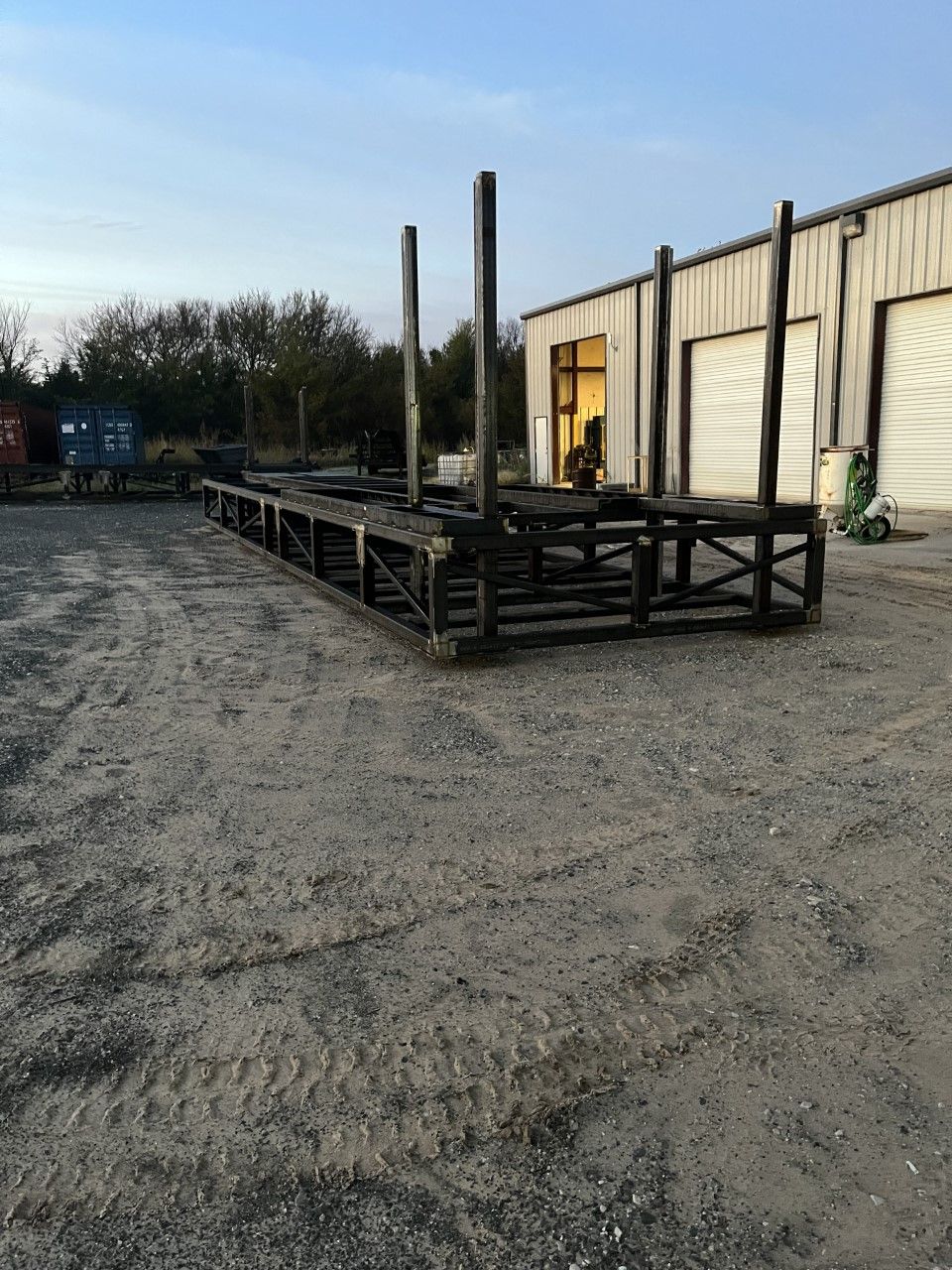 A large metal structure is sitting in the dirt in front of a building.