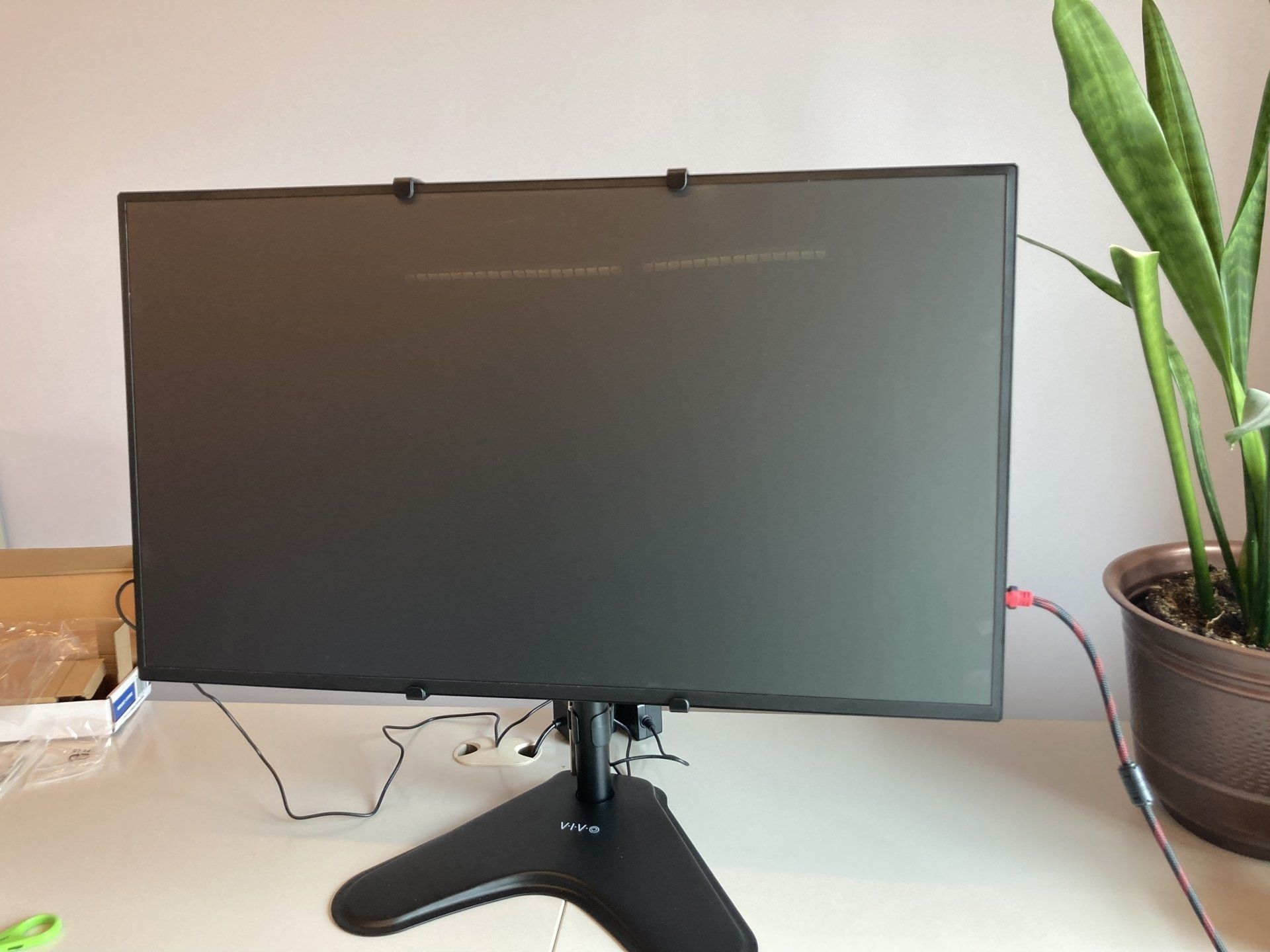 A computer monitor is sitting on a desk next to a potted plant.