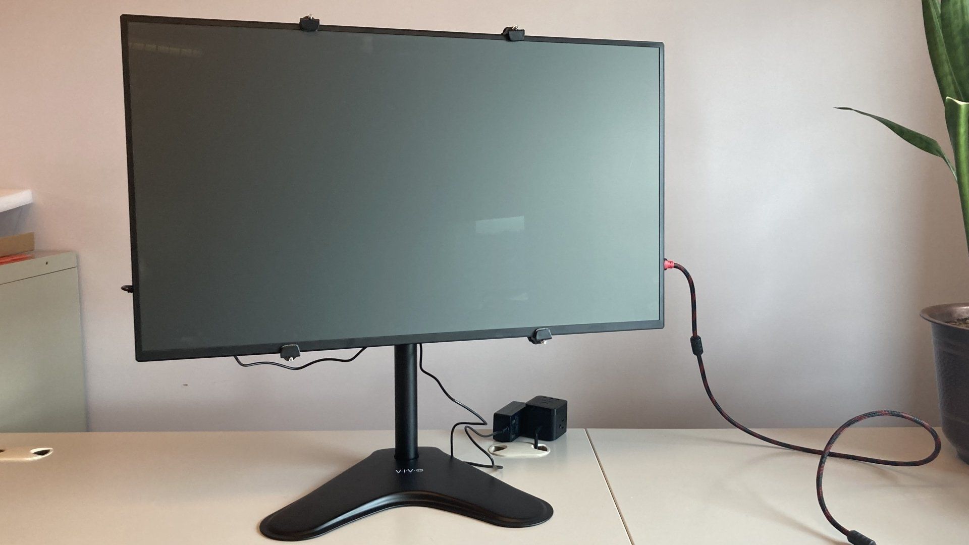 A computer monitor is sitting on a desk next to a plant
