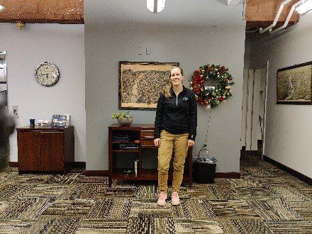 A woman is standing in a room with a wreath on the wall.