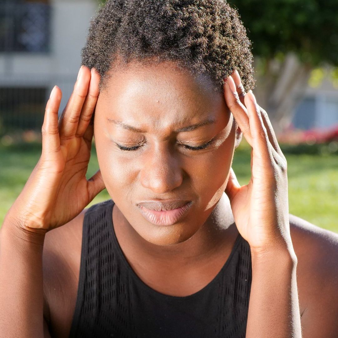 A woman in a black tank top is holding her head