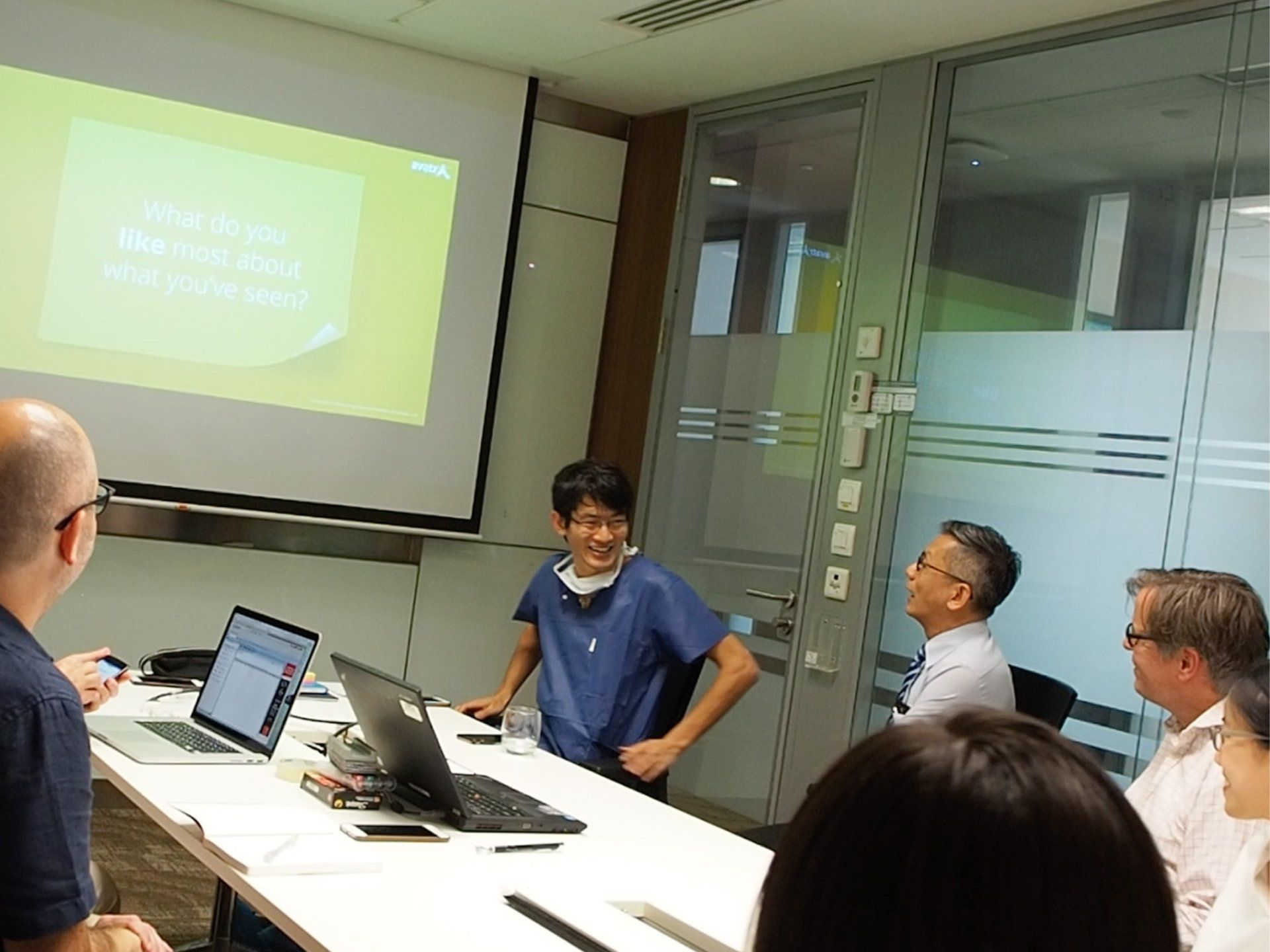 a group of people are sitting around a table with laptops in front of a projector screen .