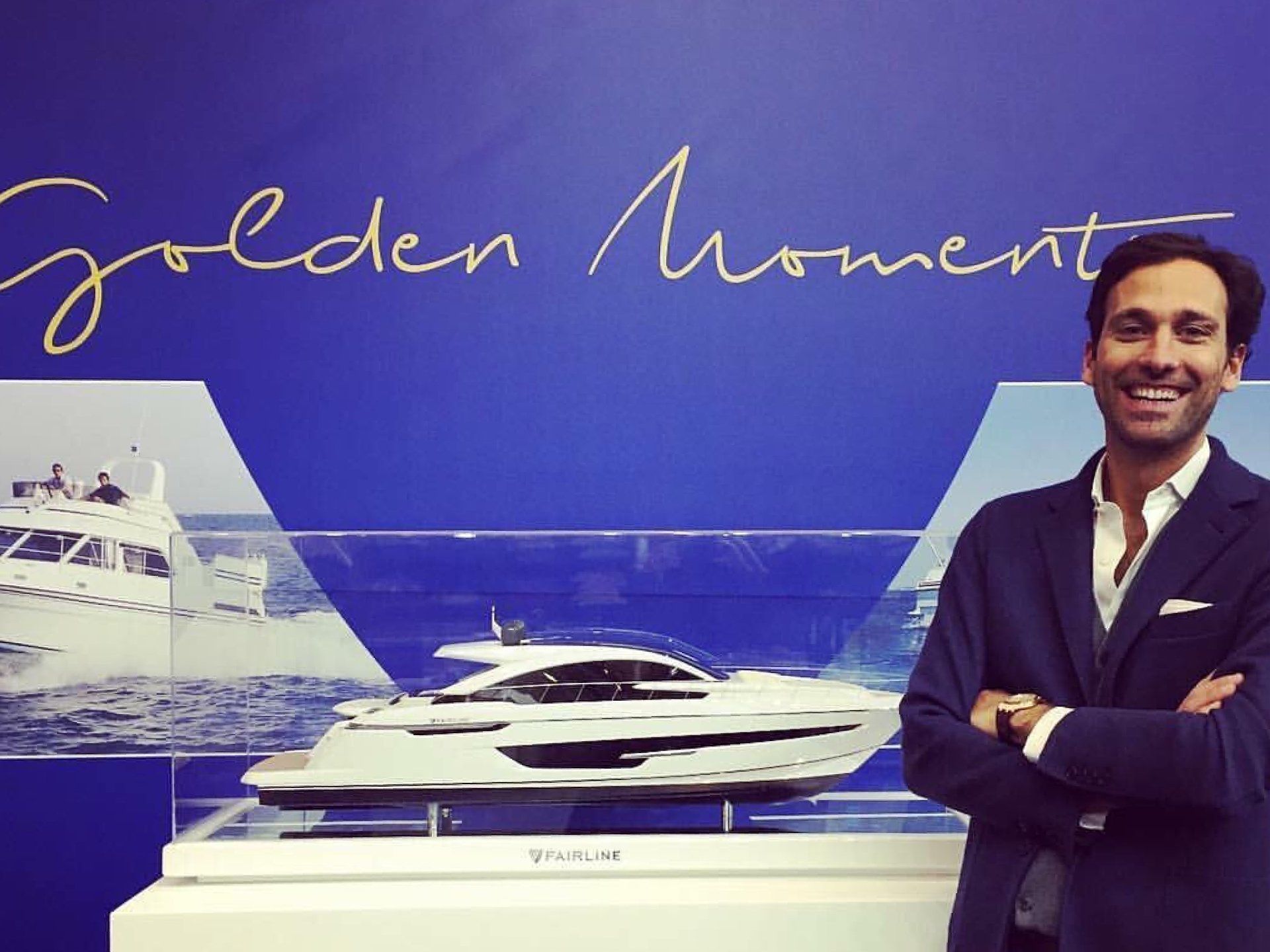 A man in a suit stands in front of a golden moment sign