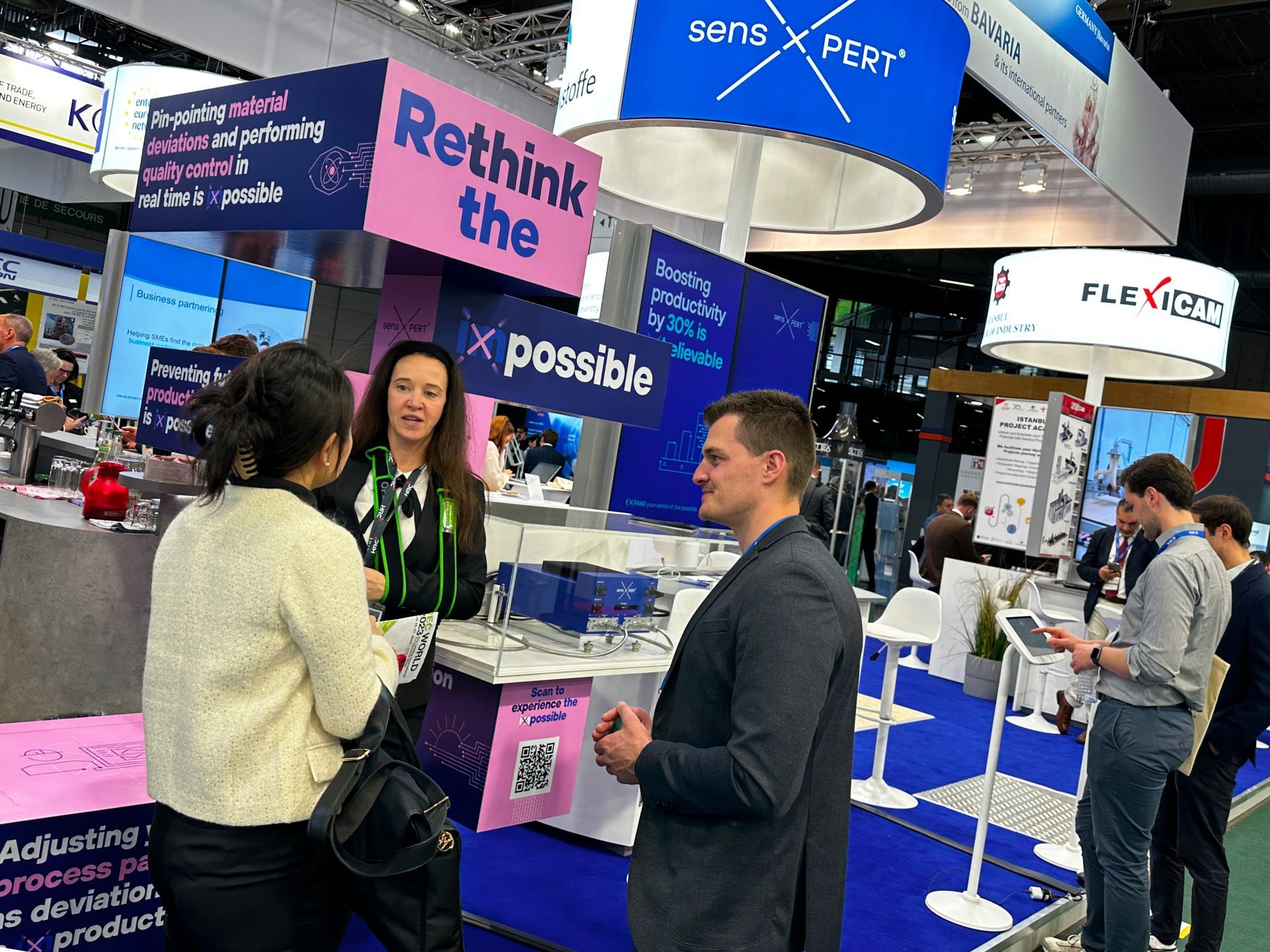 a group of people are standing in front of an event stand for sensXPERT that says rethink the possible .
