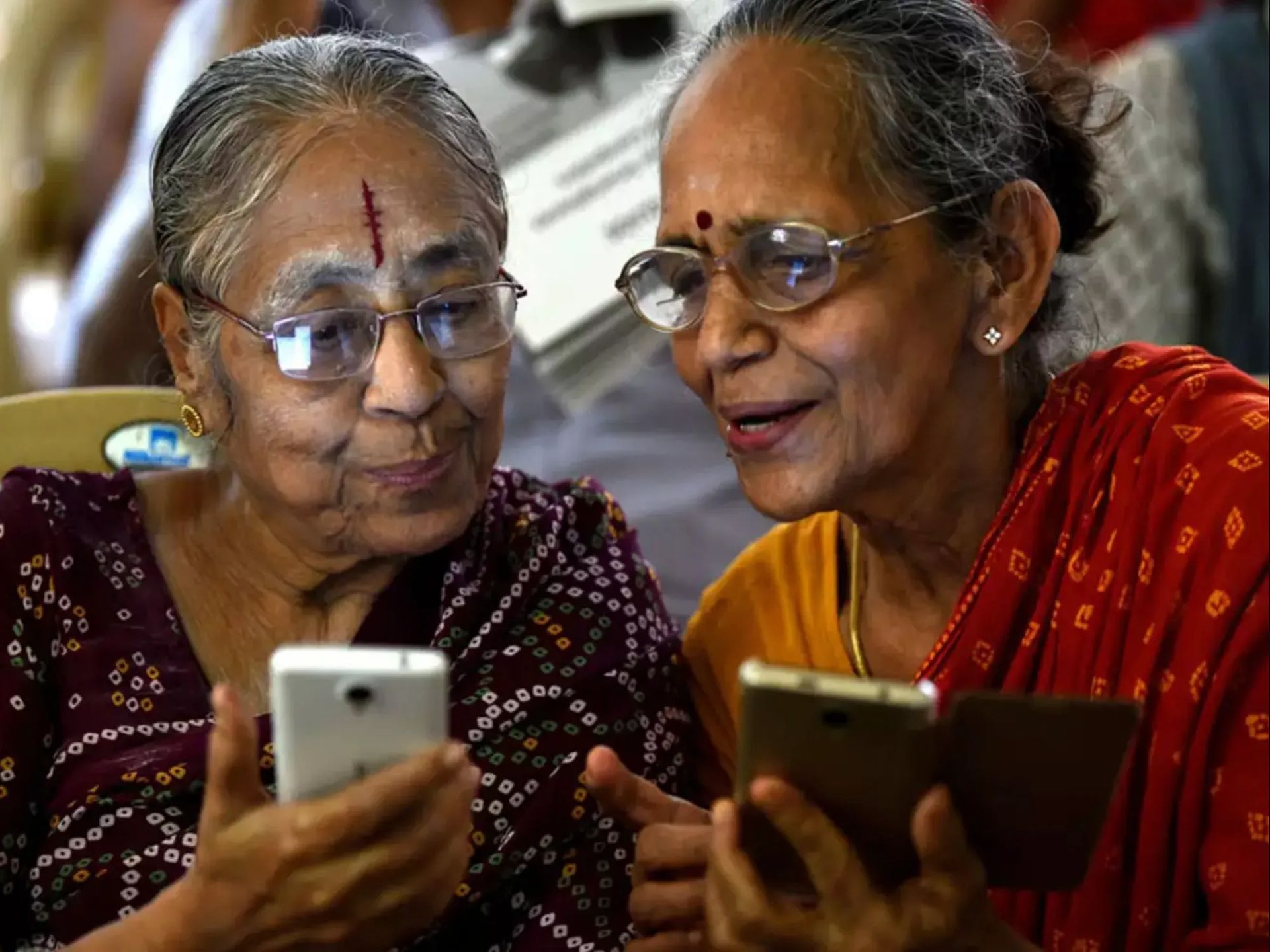 two older women are looking at a cell phone together .
