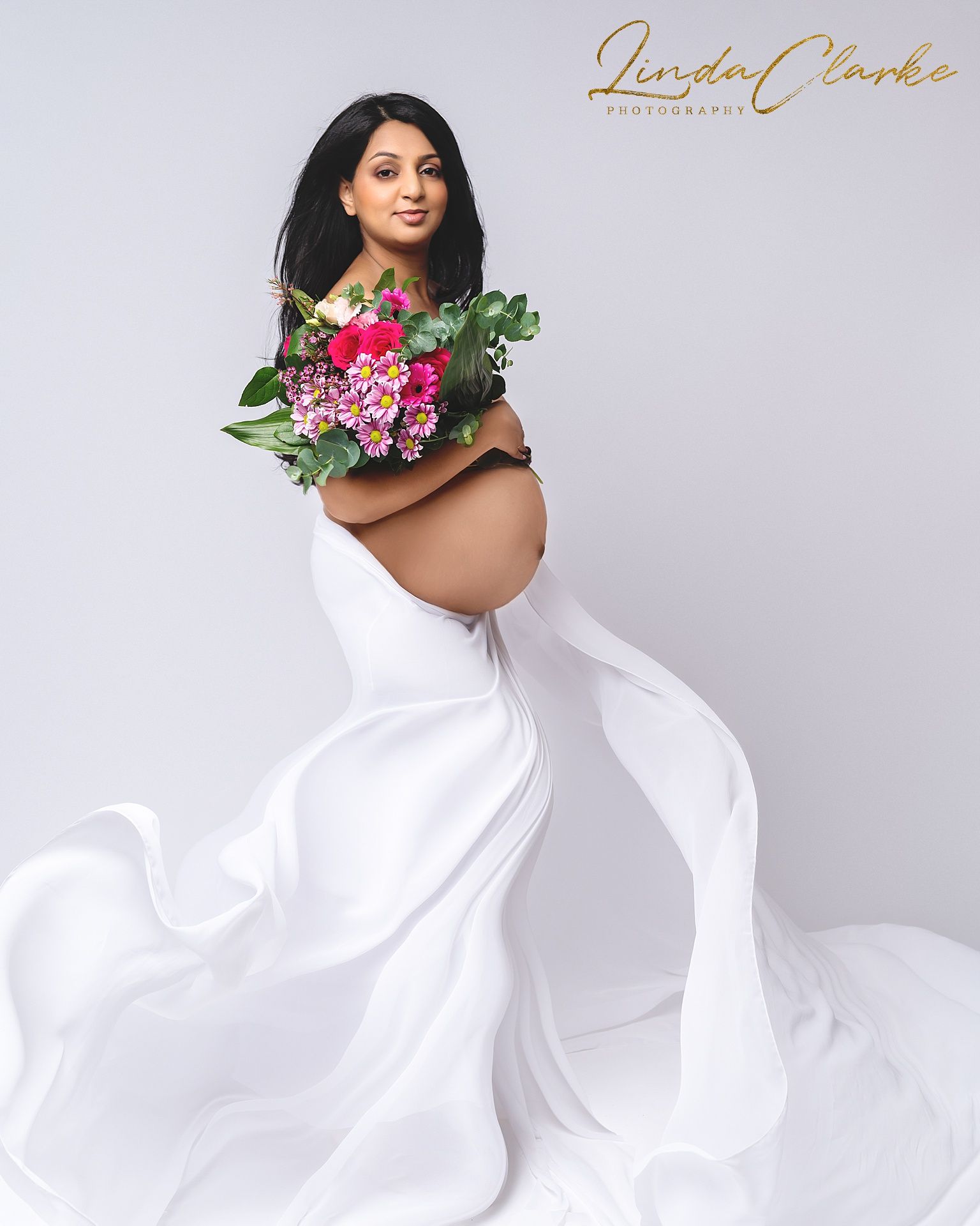 Pregnant woman wearing a white dress and holding a bouquet of flowers