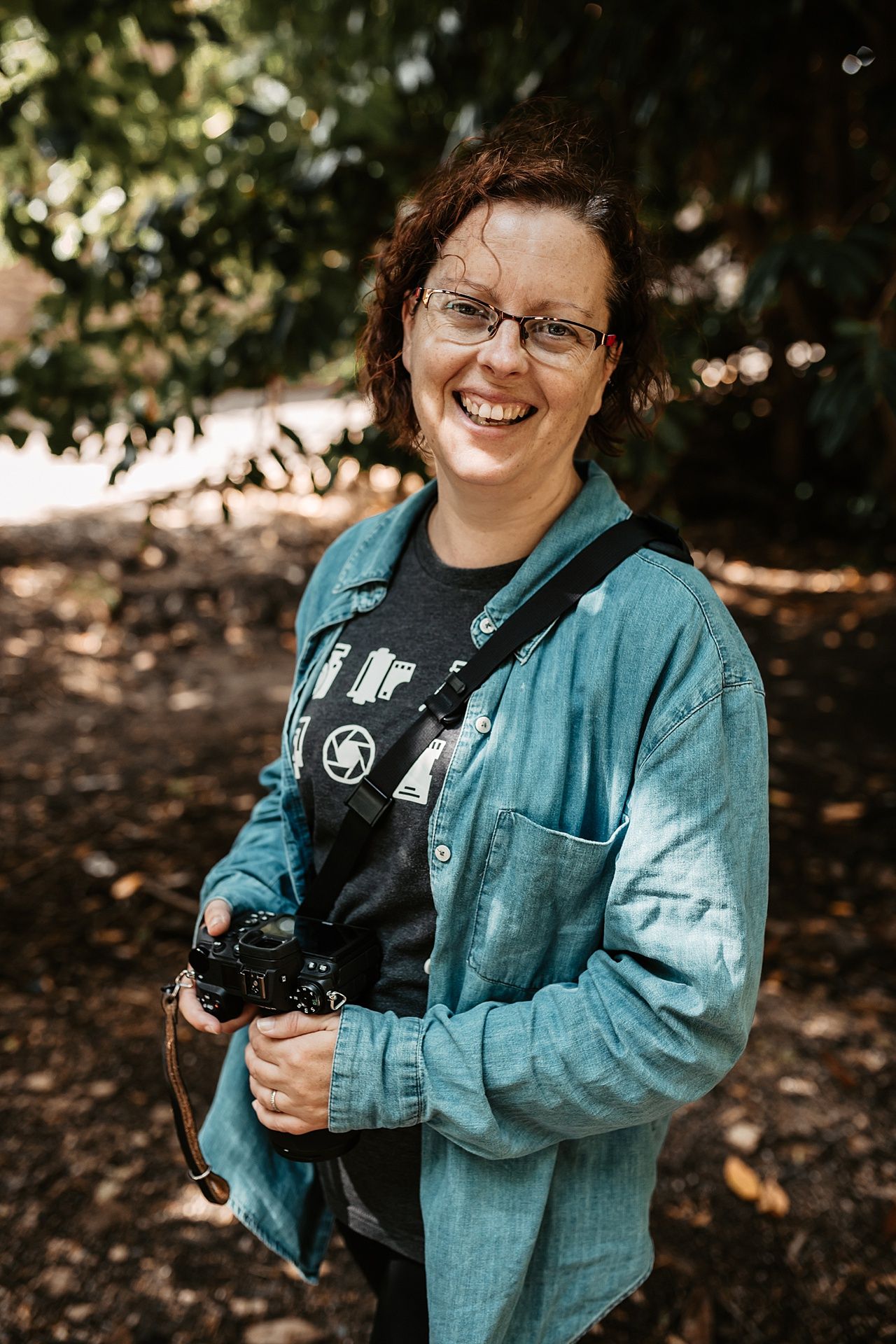 A women smiling and holding a camera in the woods