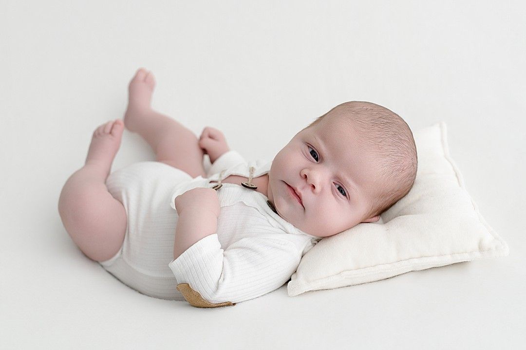 Awake newborn baby lying comfortably on a soft cushion during a calm, baby-led newborn photography session in a Dublin studio.