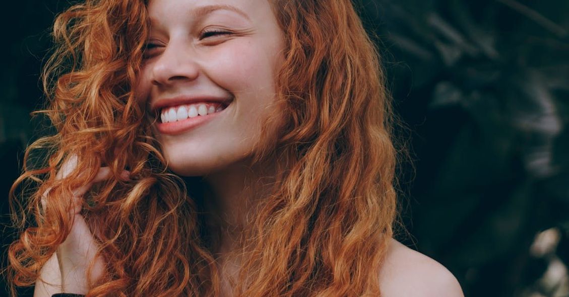 A woman with red curly hair is smiling and looking at the camera.