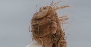 A woman with long hair blowing in the wind covering her face.