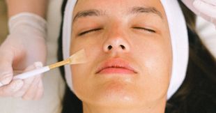 A woman is getting a facial treatment with a brush on her face.