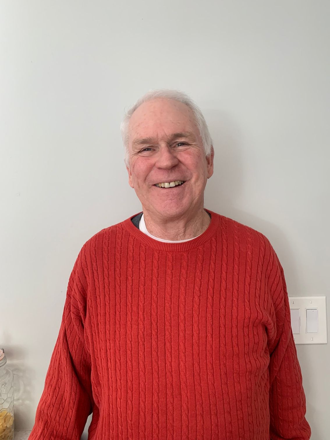 Gray-haired man in red shirt grinning.