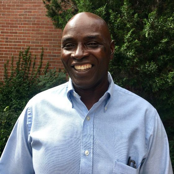 A cheerful photo of Patrick Lutalo wearing a blue shirt, displaying a warm smile.