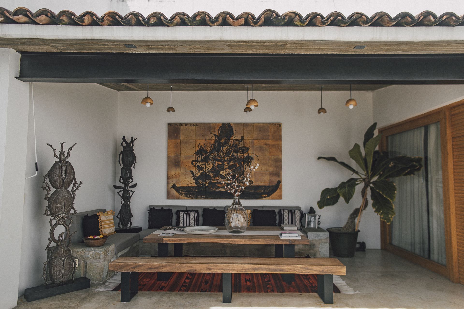 Outdoor patio with wood furniture, art, and plants under a white ceiling and exposed beams.
