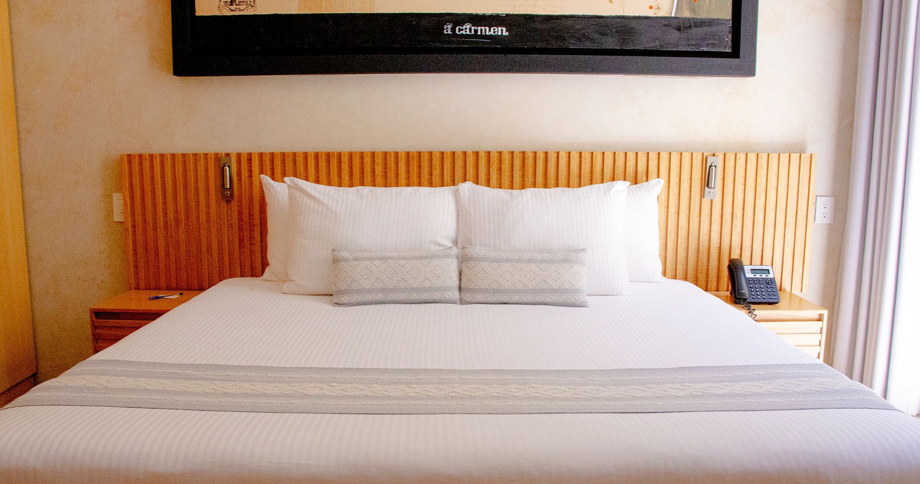 Hotel bed with white linens, wooden headboard, two nightstands, and a large black framed artwork.