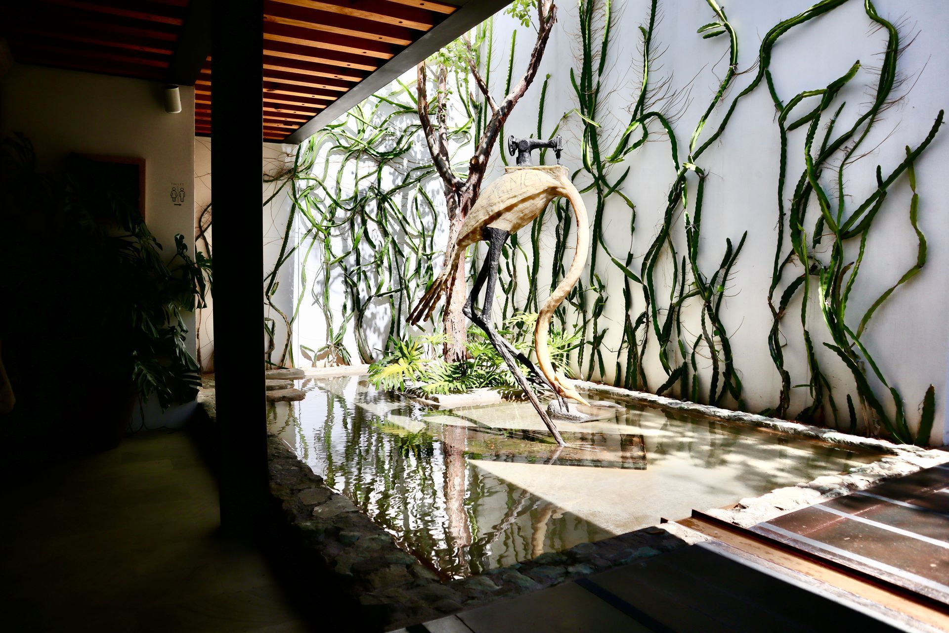 White-walled courtyard with tree, staircase, and bench. A metal bridge extends overhead.