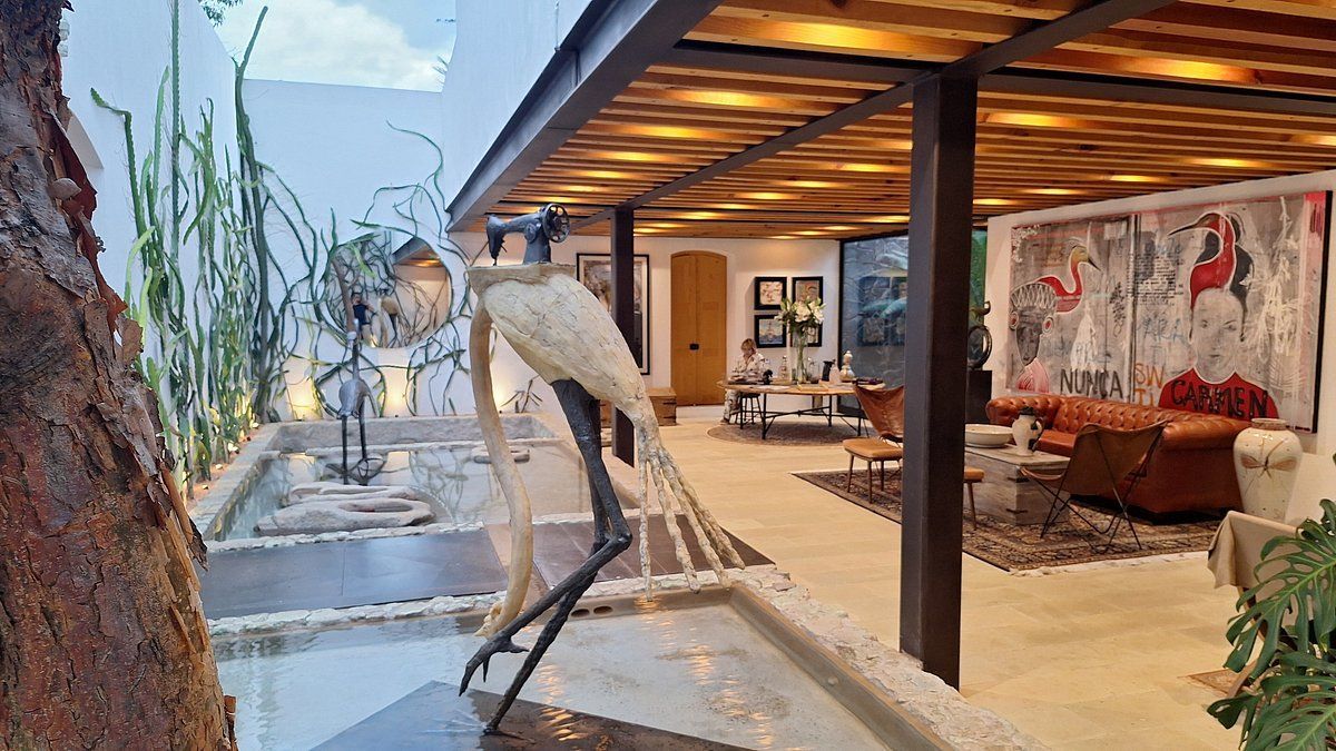 Outdoor art gallery, sculpture of a bird in a reflecting pool, wood-paneled ceiling, artwork on the walls.