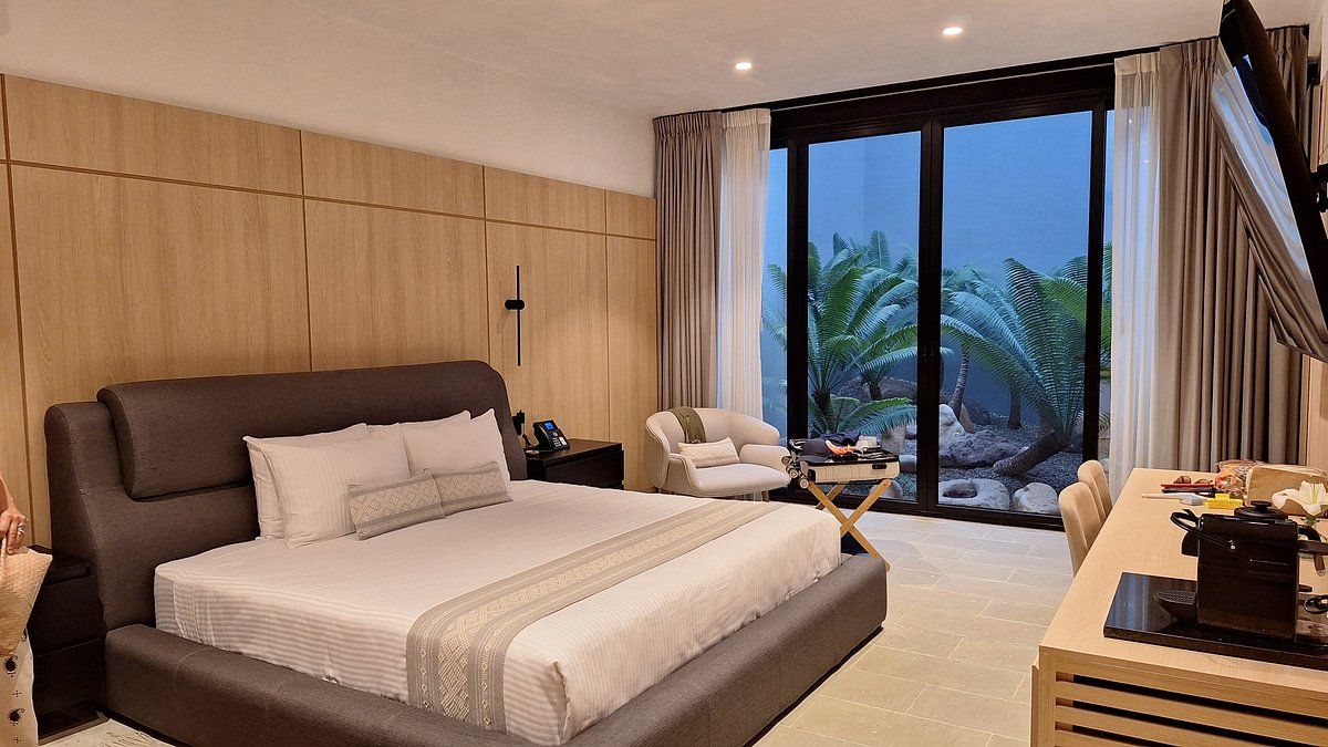Modern bedroom with large bed, wooden paneling, and a view of a garden through a large window.