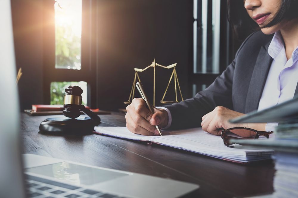 A Woman Is Sitting At A Desk Writing On A Piece Of Paper — SJP Law In Buderim, QLD
