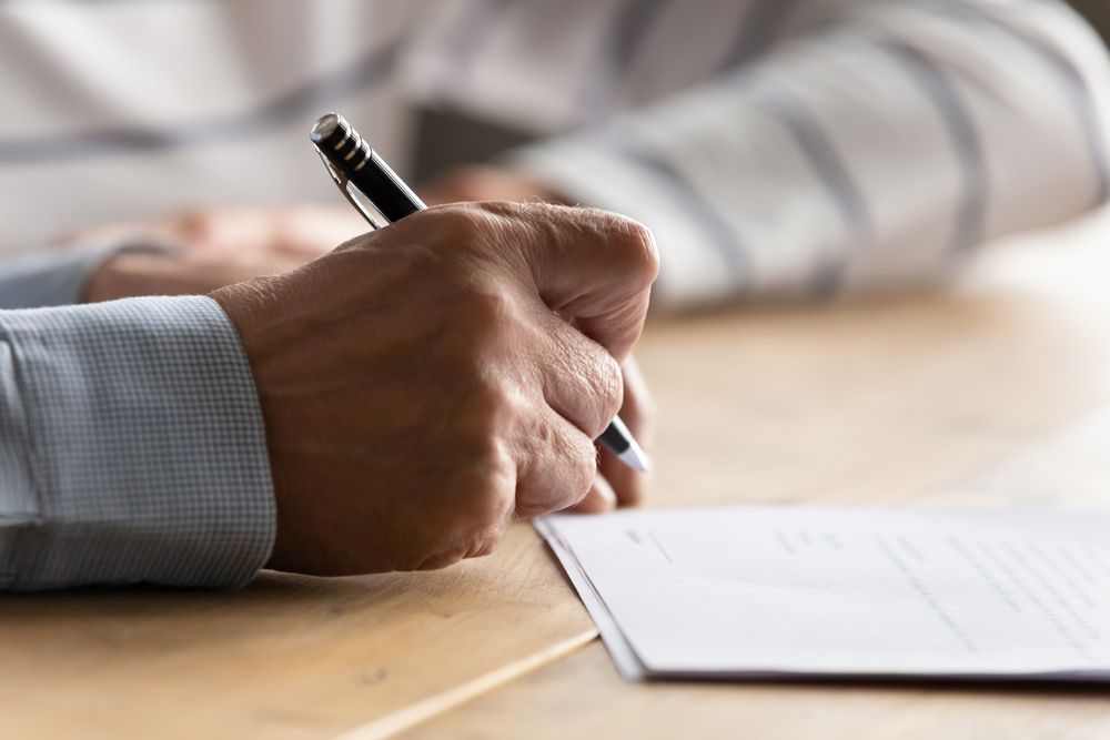 A Man Is Writing On A Piece Of Paper With A Pen — SJP Law In Coolum Beach, QLD