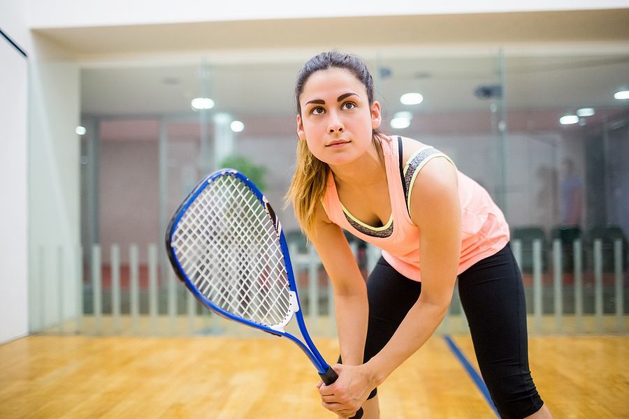 A woman is holding a squash racket on a court.