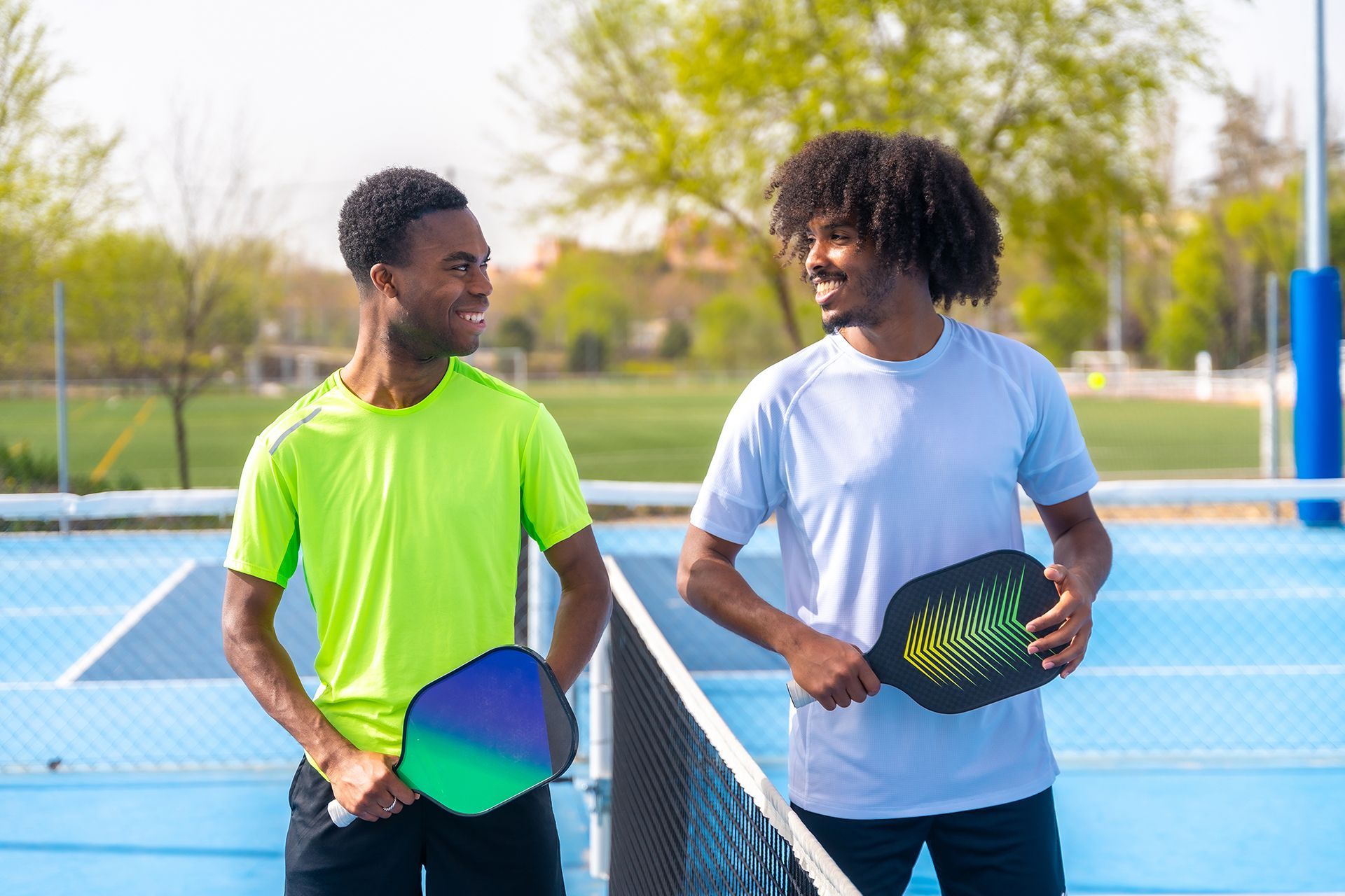 Two men are standing next to each other on a tennis court holding paddle rackets.