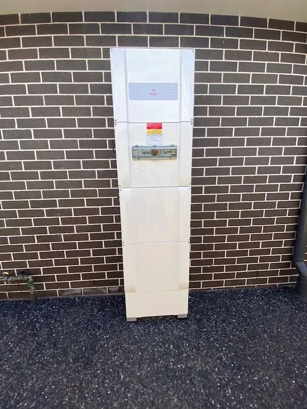 White Electrical Box Mounted Against a Dark Brown Brick Wall — KACE Electrical Solutions In Ramsay, QLD