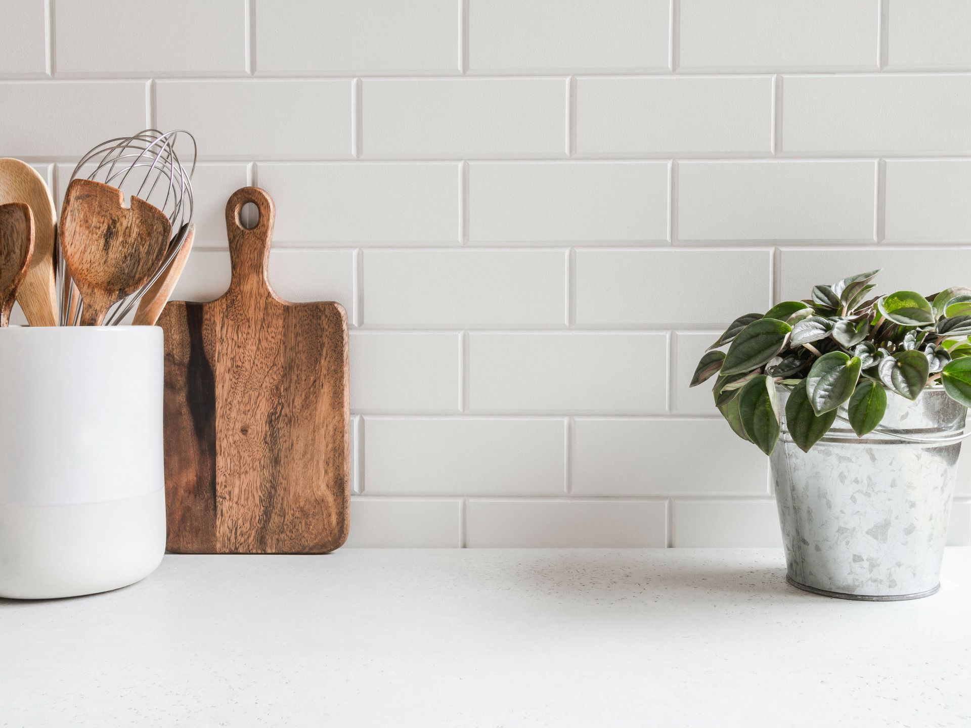 A kitchen counter with utensils , a cutting board , and a potted plant.