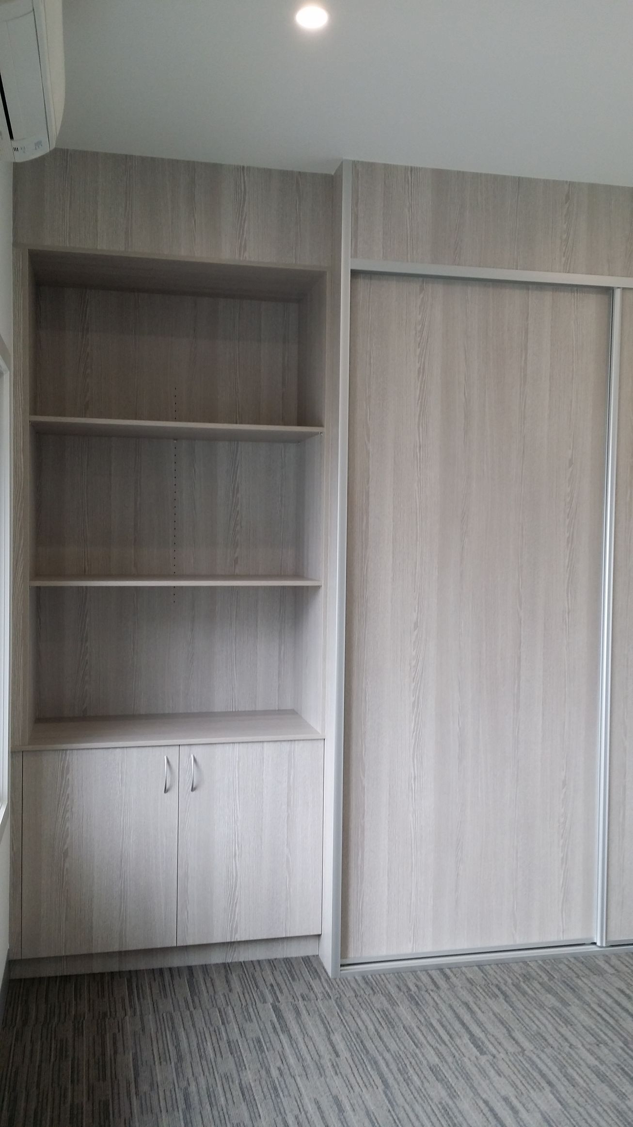 A room with a sliding door , shelves , cabinets and a window.