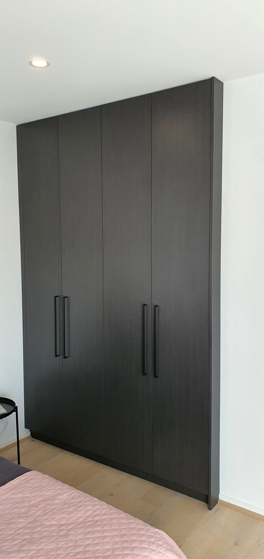 A bedroom with a large black wardrobe and a bed.