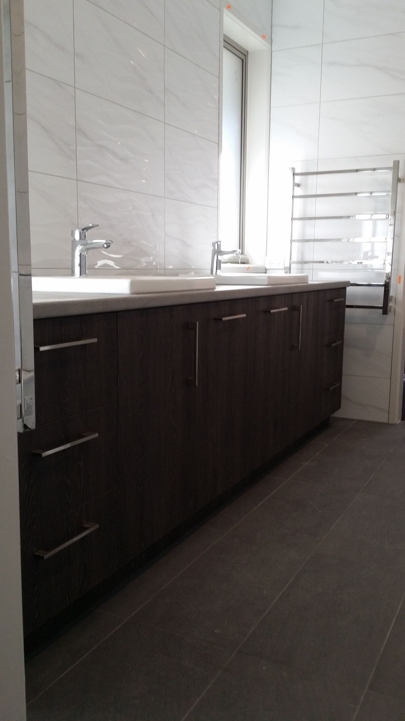 A bathroom with two sinks , a towel rack and a window.