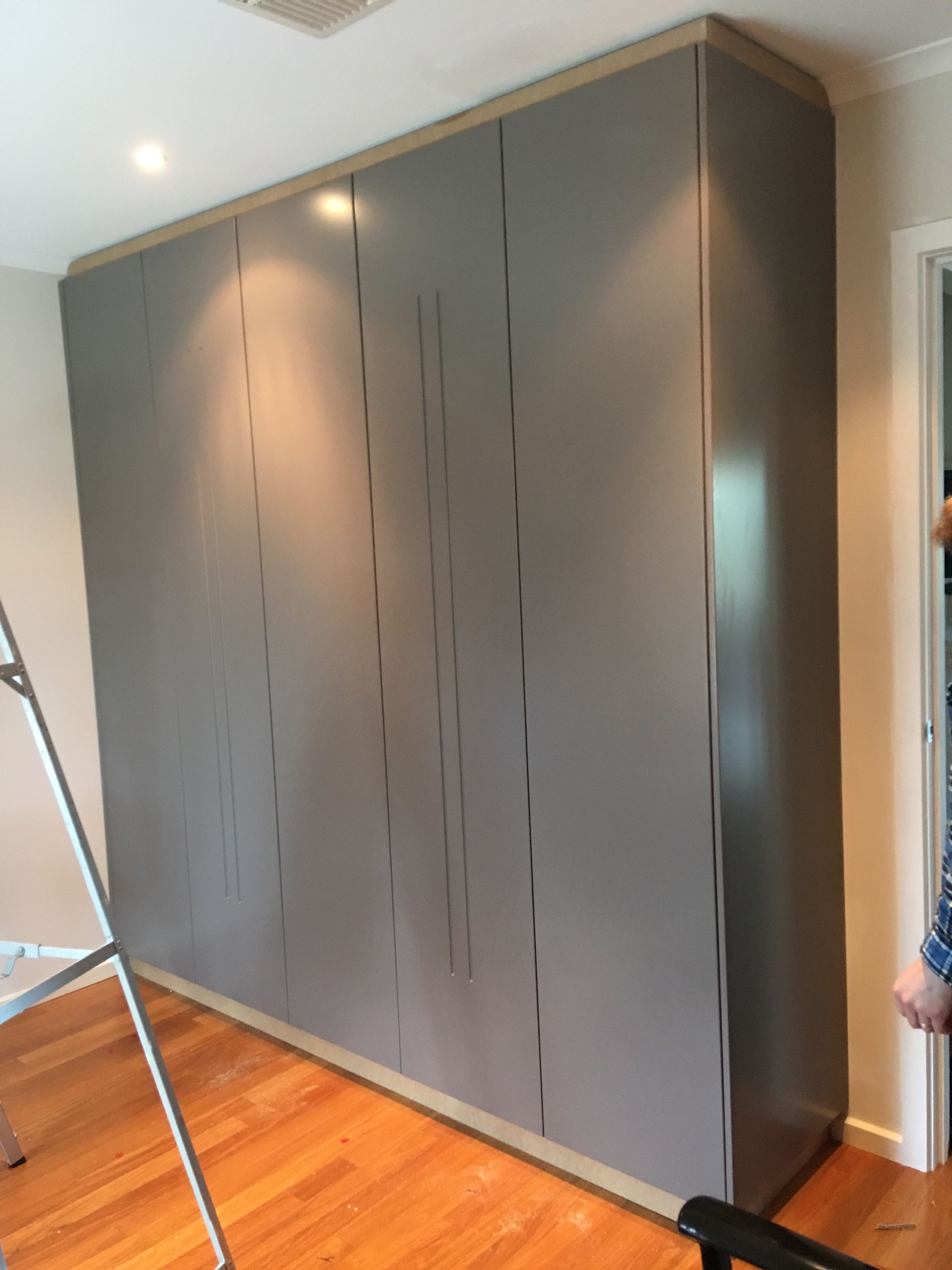 A ladder is sitting in front of a large grey cabinet