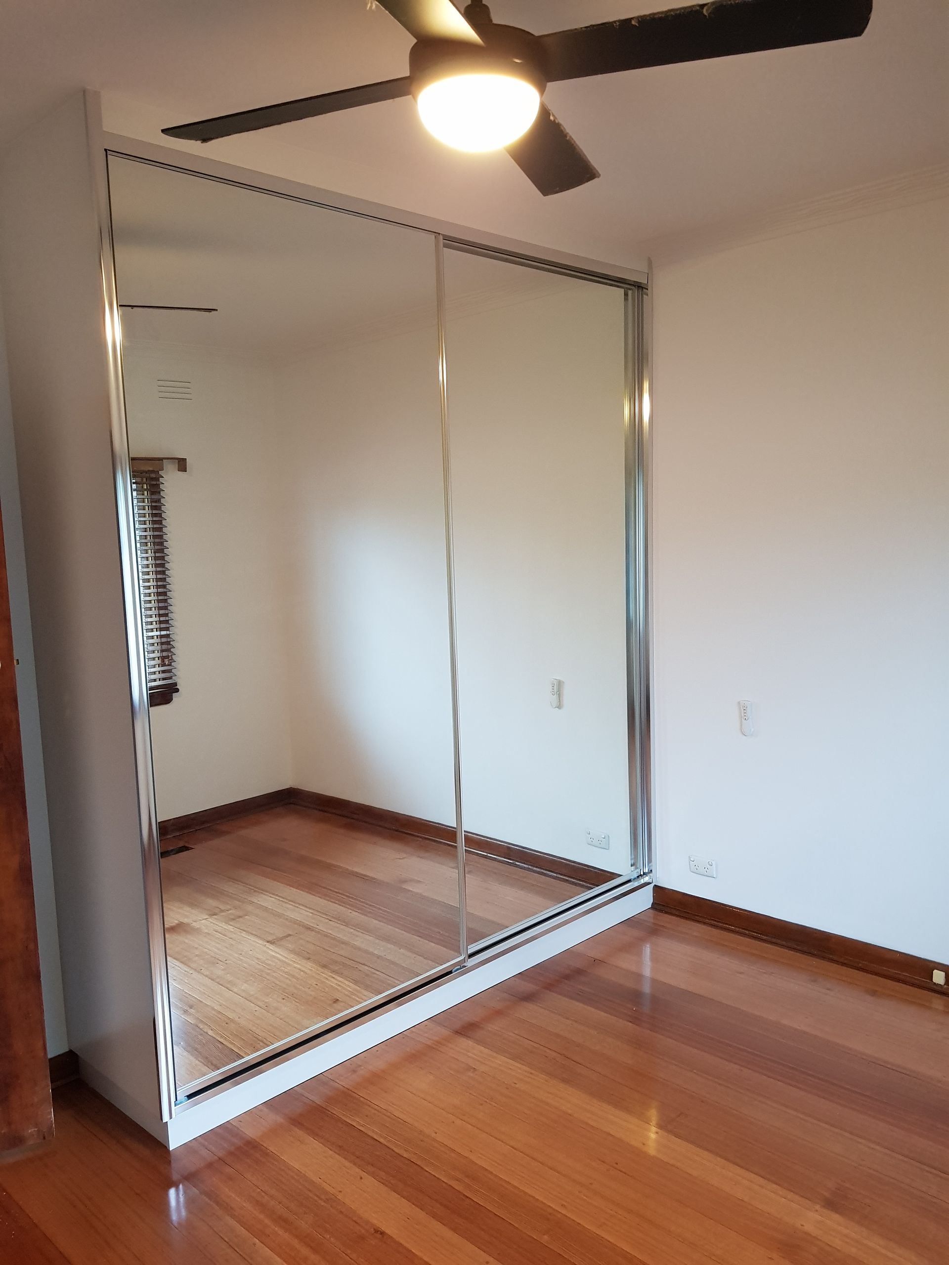 A bedroom with a large mirrored wardrobe and a ceiling fan.