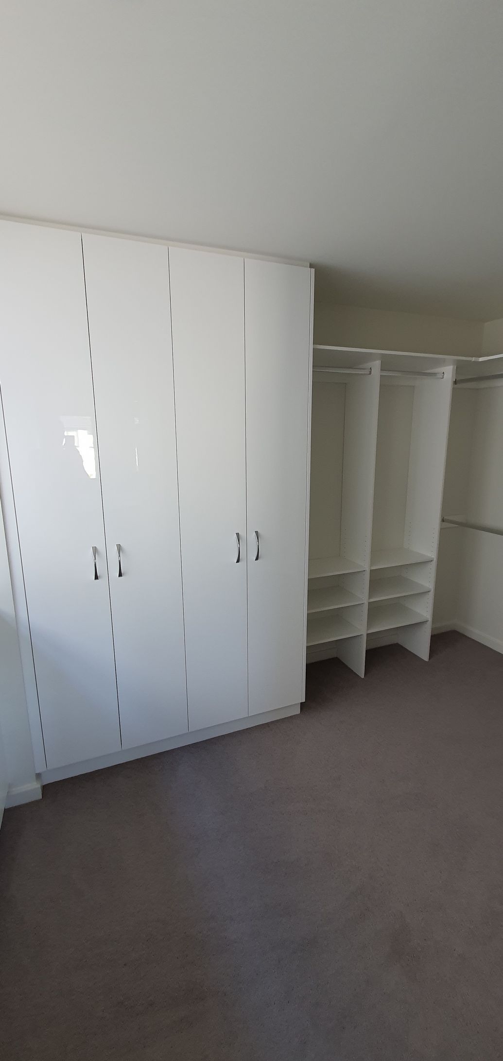 An empty walk in closet with white cabinets and shelves.
