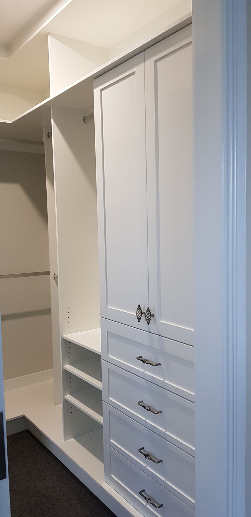 A walk in closet with white cabinets and drawers.