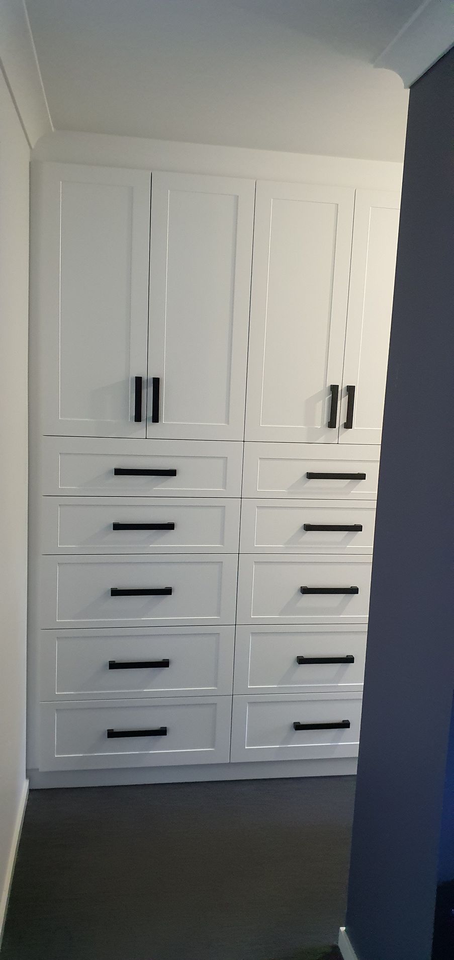 A room with white cabinets and drawers with black handles.