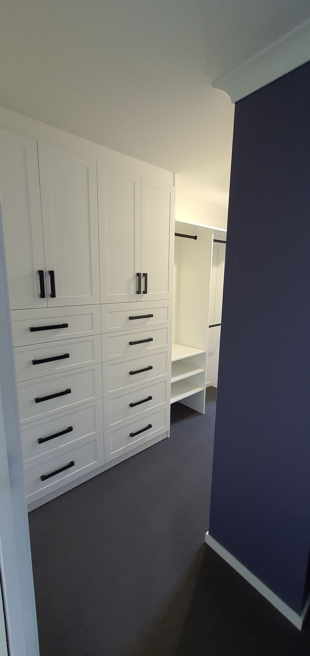A walk in closet with white cabinets and drawers and a purple wall.