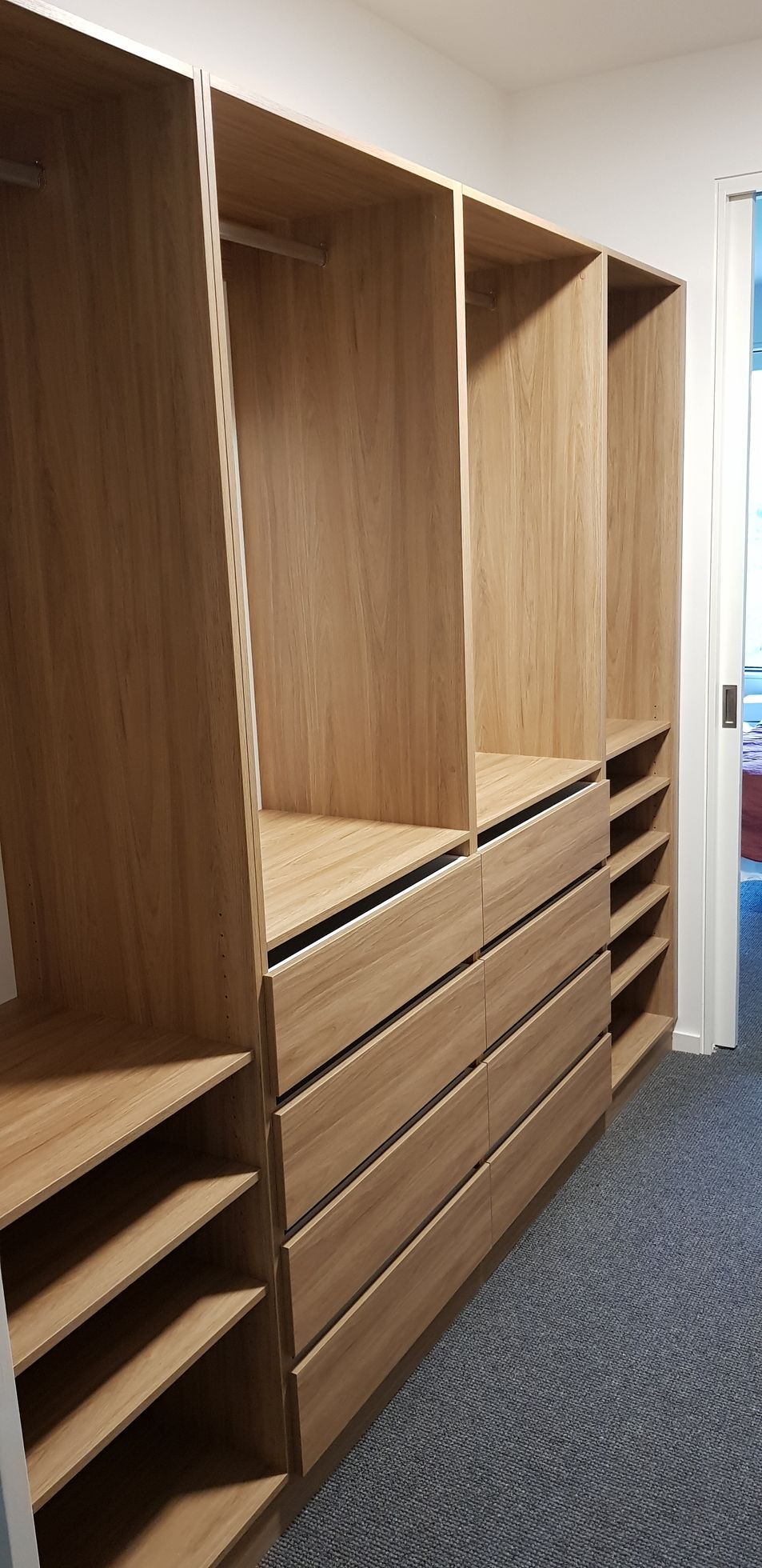 A walk in closet with lots of wooden shelves and drawers.