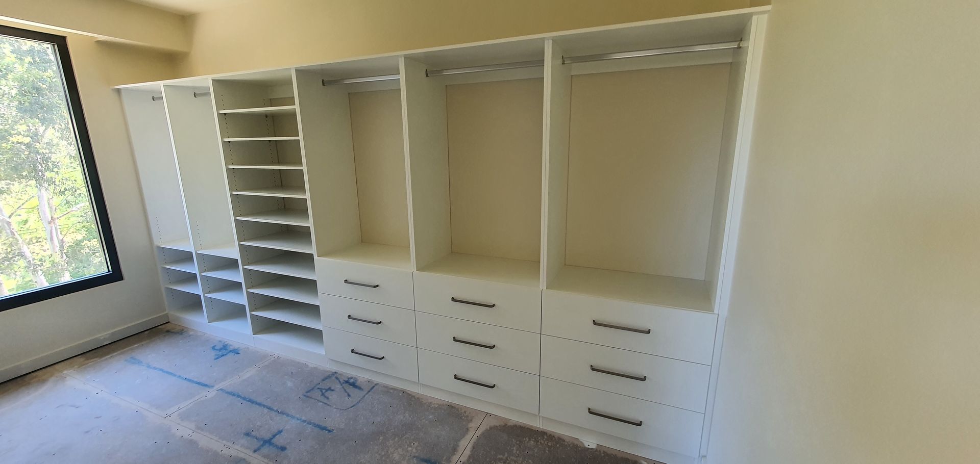 A large closet with lots of shelves and drawers in a room with a window.