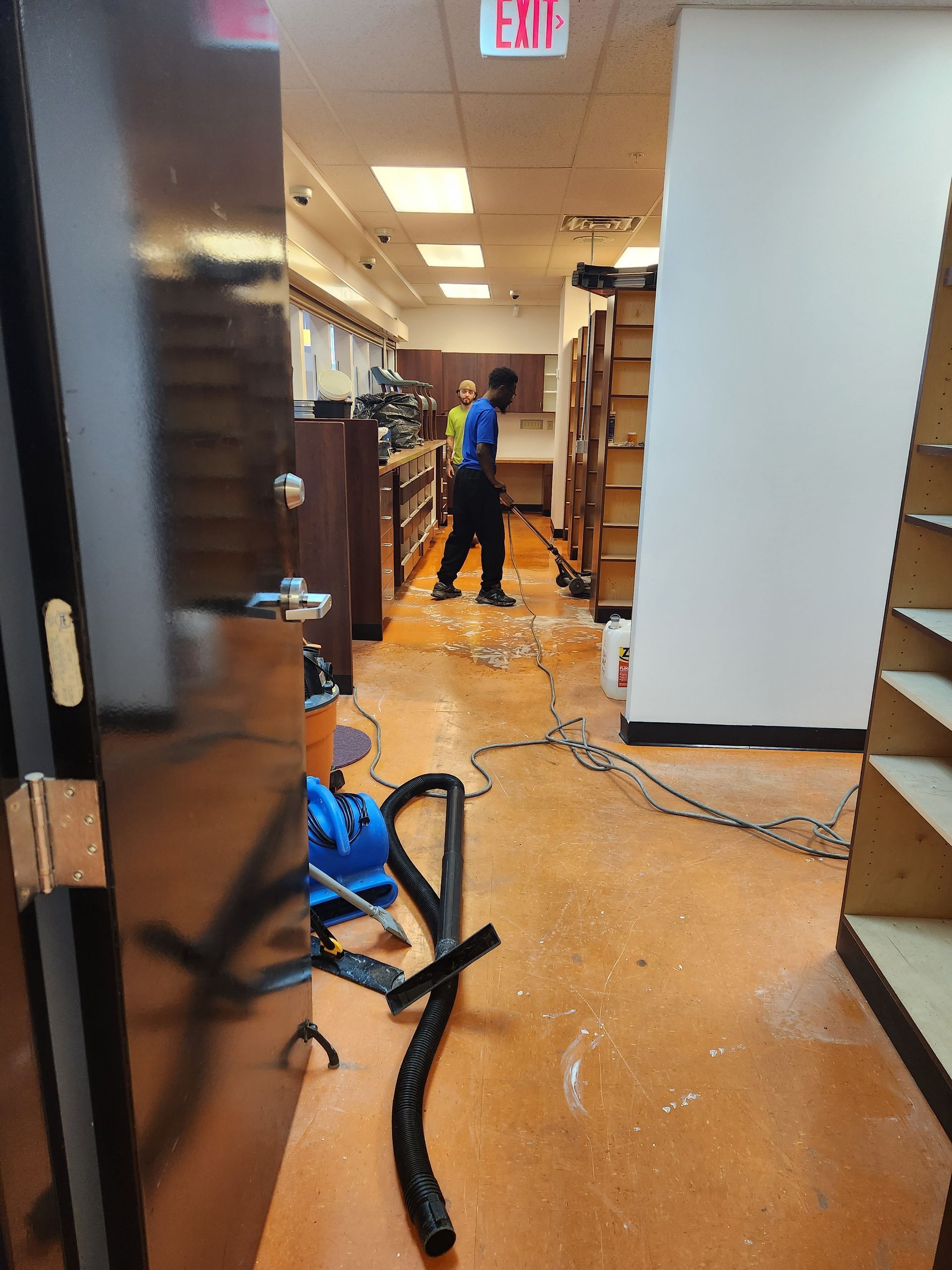 Workers use industrial cleaning equipment to dry a flooded room with orange flooring.