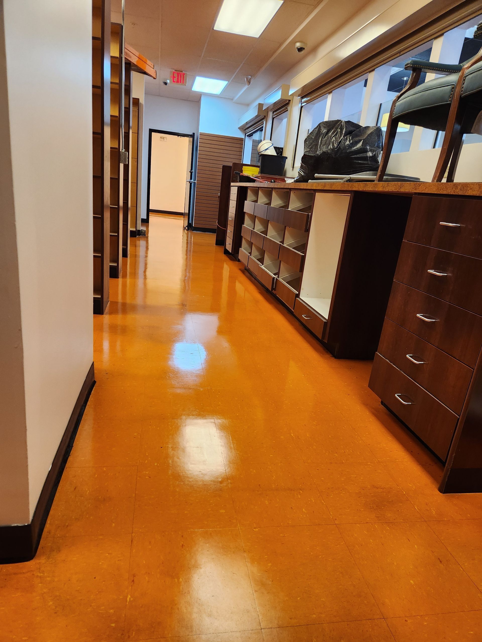 A hallway with shiny orange flooring, a white wall on the left, and dark wooden shelving units along the right side.