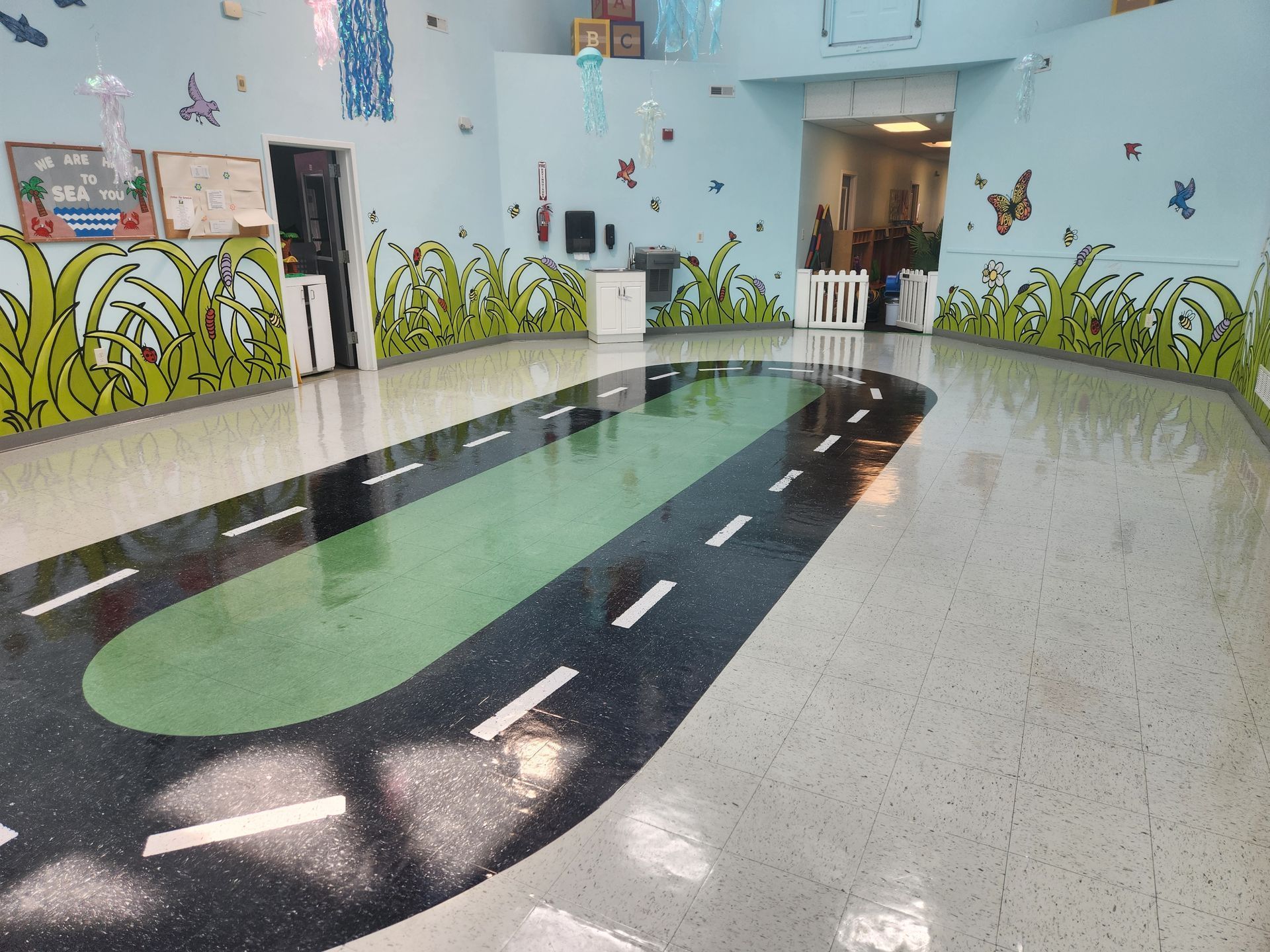 A brightly colored, kid-friendly indoor play area with a painted racetrack on the floor and mural-painted walls.