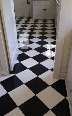 A kitchen floor with a glossy black and white checkerboard tile pattern, viewed from a doorway.