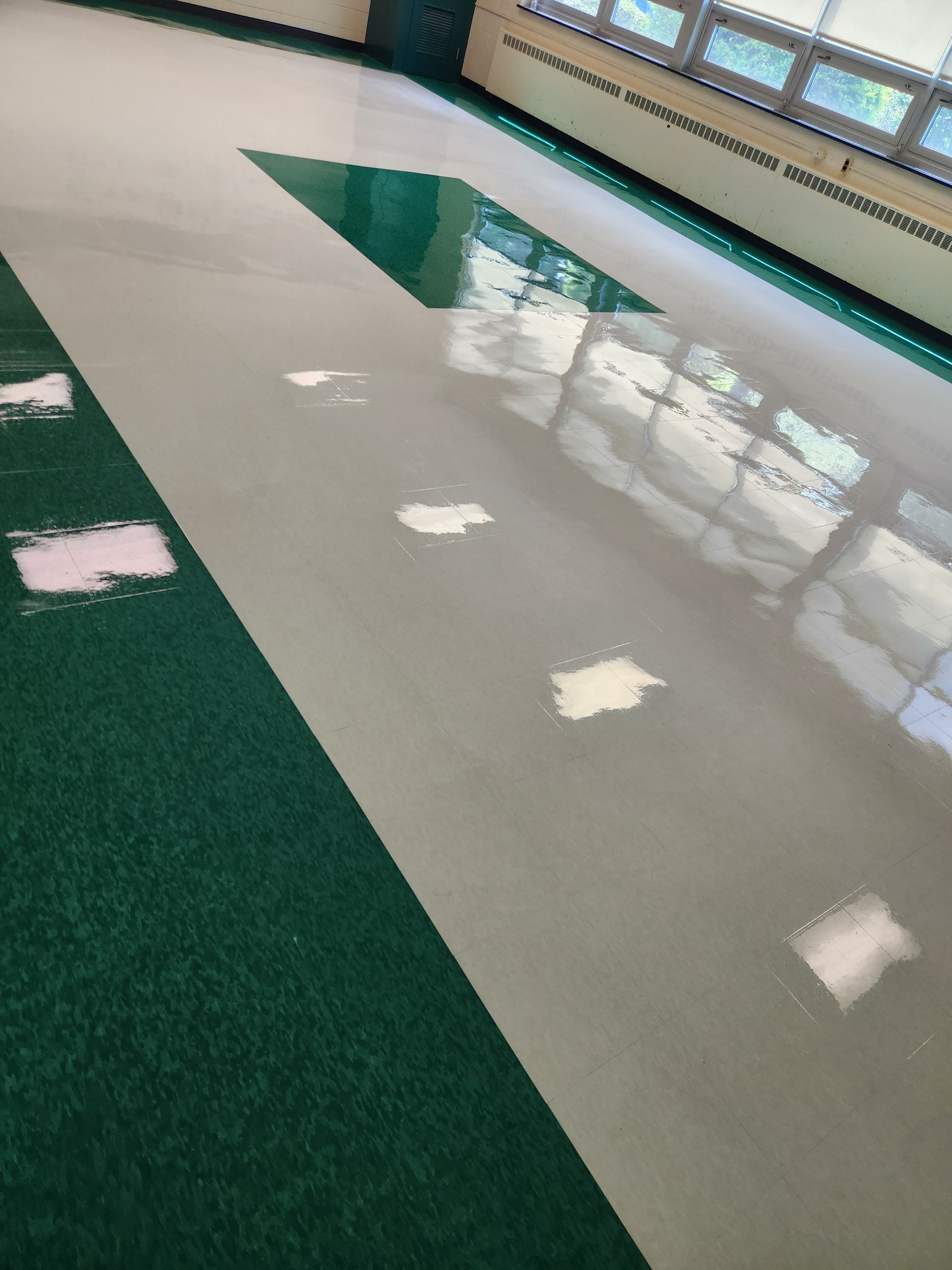A shiny, light-gray floor in a room, featuring a large green section and scattered white scuff marks.