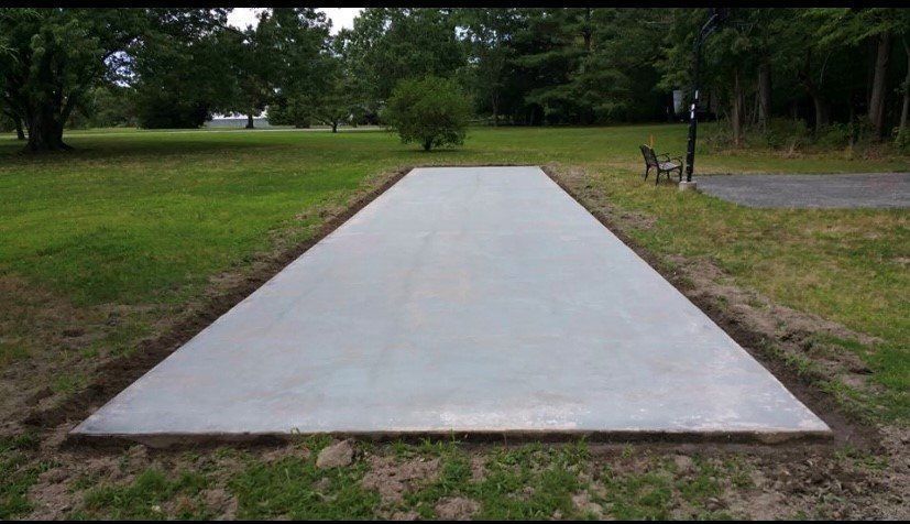 A rectangular concrete slab set in a grassy yard, surrounded by an open lawn and trees.