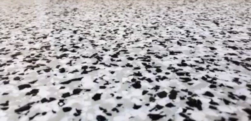A close-up of a speckled floor coating with black, white, and gray flakes embedded in a smooth, light-colored resin finish.