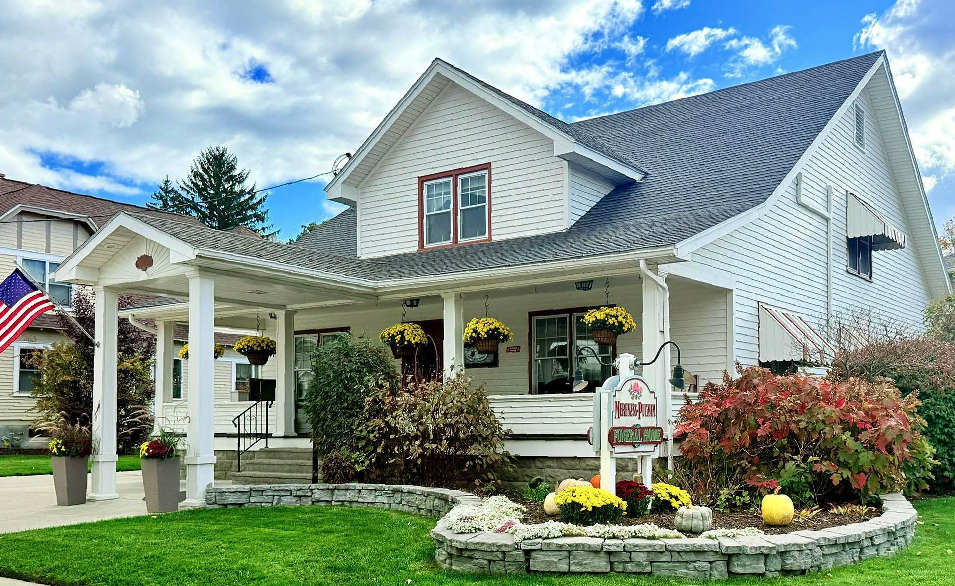 A white house with a porch and an american flag in front of it.