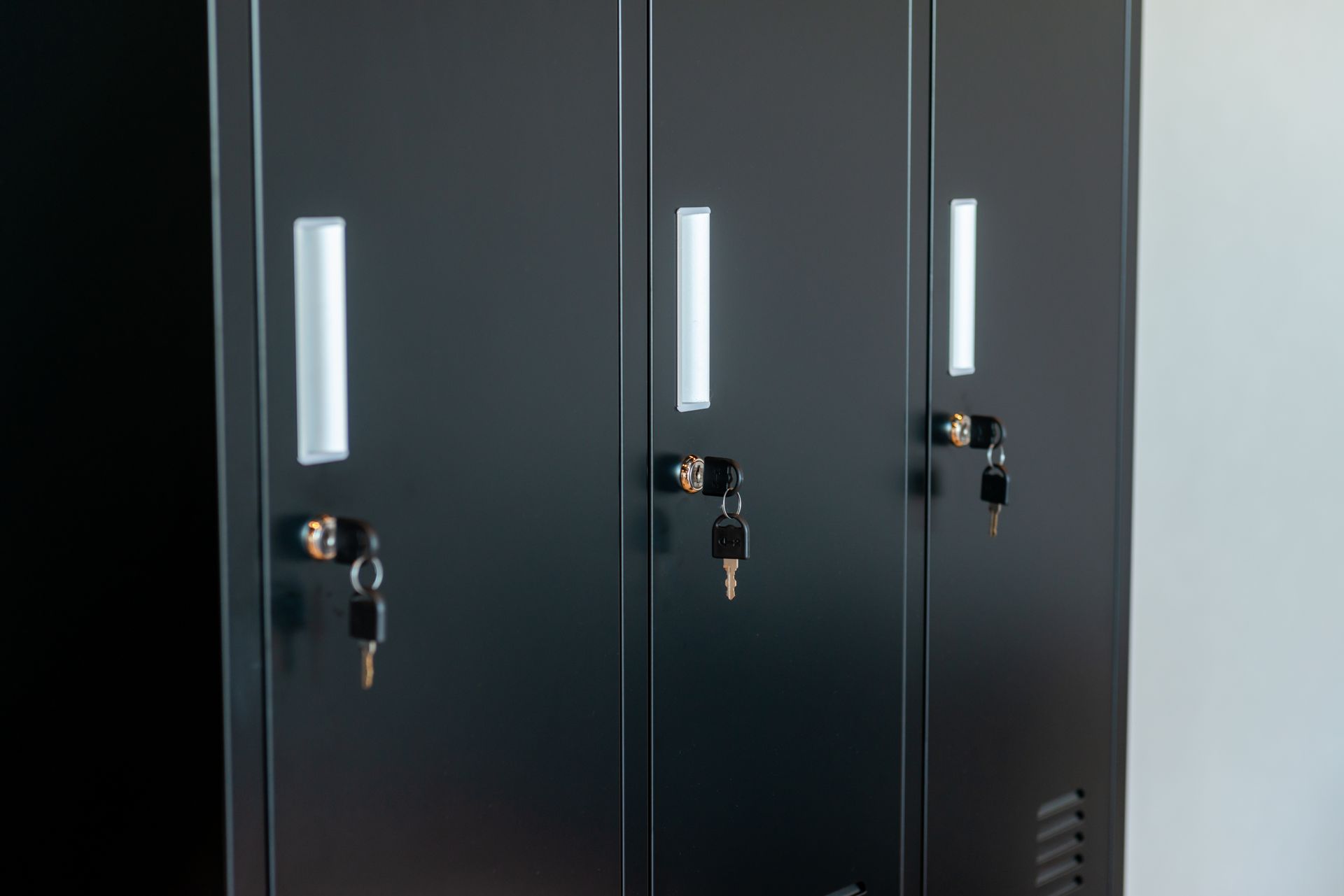 Three black metal lockers with silver handles, each with a key in the lock. Three black metal lockers with silver handles, each with a key in the lock.